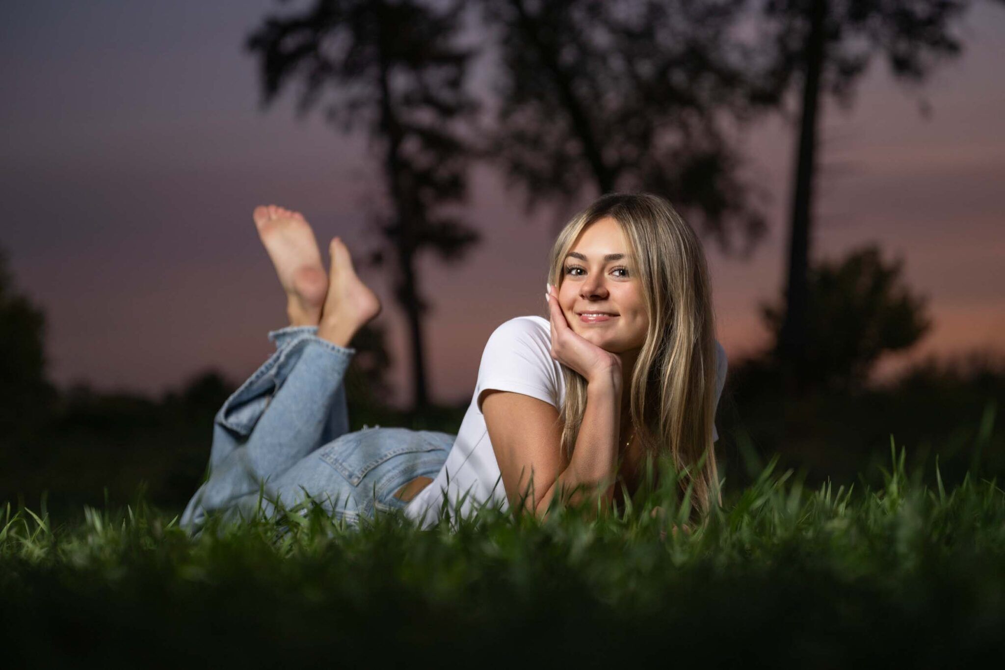 High school senior girl laying on ground with beautiful sunset background.